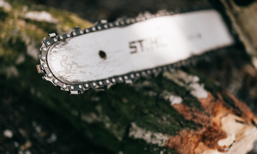 A close up of a Stihl chainsaw resting against a log.