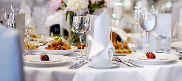 A fully stocked banquet table with glassware, linens and plates.